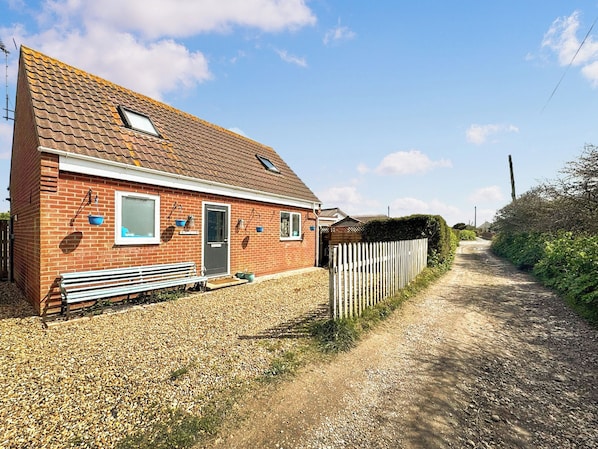 A brick house with a gravel driveway, a wooden fence, and a bench.