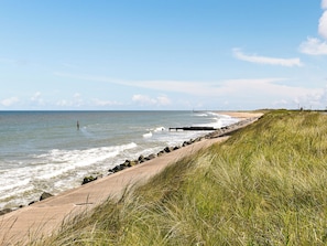 A coastal walkway with a grassy embankment, a sandy beach, and the ocean.