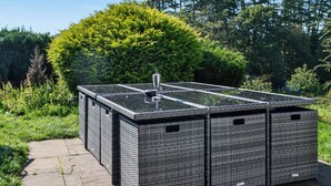 A large, dark-colored outdoor structure with a flat roof, possibly a gazebo or a covered patio area, surrounded by lush greenery and trees. - The Granary - UK45181 (Newcastleton)