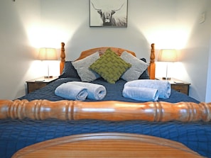 A neatly made bed with rolled towels, a wooden headboard, and two bedside lamps. - 3 bedroom accommodation in Coleford (Coleford)