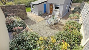 Ein zweistöckiges Haus mit Garten, einer Terrassenanlage, einem kleinen Schuppen und verschiedenen Pflanzen.