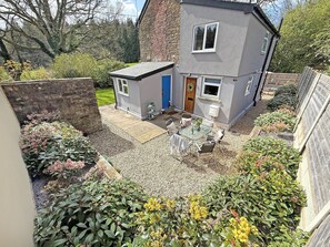A two-story house with a garden patio, a small shed, and a variety of plants.