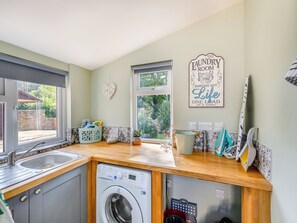 A laundry room with a washing machine, a sink, and a window.