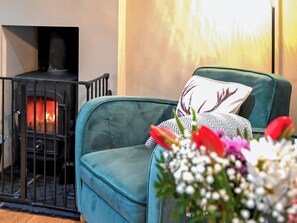 A teal armchair with a patterned pillow, a small black heater, and a vase of flowers.