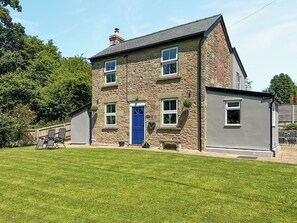 A two-story stone house with a blue door, a small garden, and a patio with chairs.