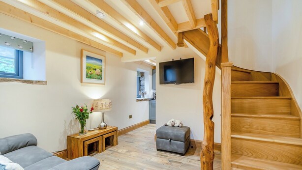 A modern living room with a wooden staircase, a sofa, a table with a lamp, and a TV mounted on the wall. - Little Pythorn - UK45253 (Westerdale, near Castleton)