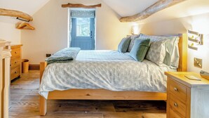 A bedroom with a sloped ceiling, wooden beams, a bed with patterned bedding, a dresser, and a window with a view. - Little Pythorn - UK45253 (Westerdale, near Castleton)