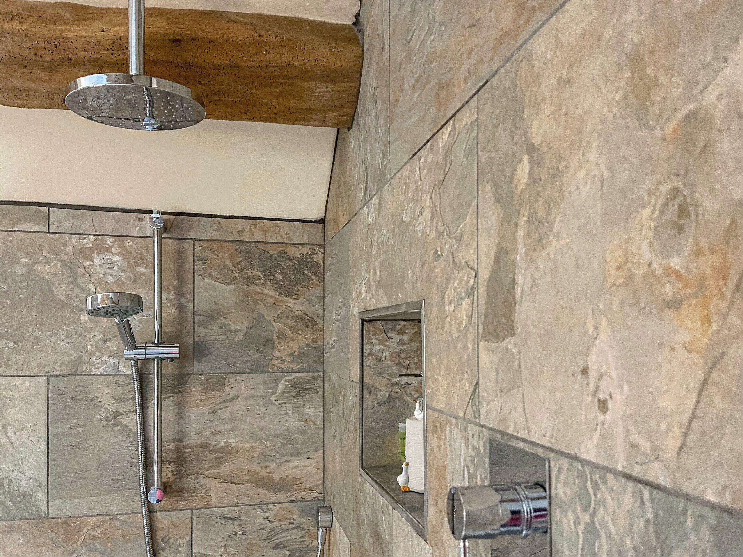 Une douche équipée d’un pommeau de douche à main et d’un robinet fixé au mur.