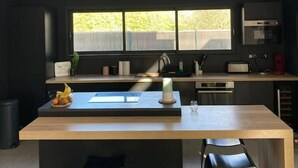 Eine moderne Küche mit einer zentralen Kochinsel, zwei schwarzen Stühlen, einem Fenster über der Spüle und Blick ins Grüne.