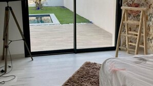 Ein Schlafzimmer mit einer großen Schiebeglastür, die auf einen Balkon mit Blick auf Bäume und eine Rasenfläche führt.