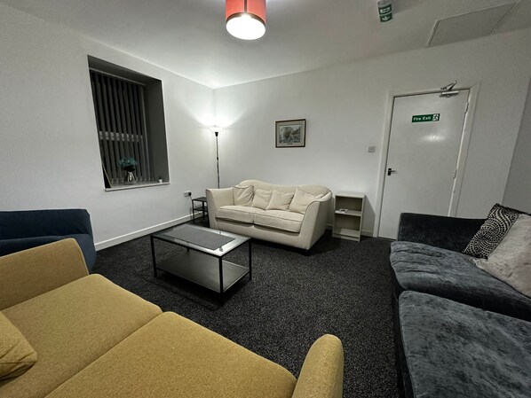 A modern living room with a beige sofa, a yellow armchair, a dark armchair, a coffee table, and a floor lamp. - Blackwood Residence (Accrington)