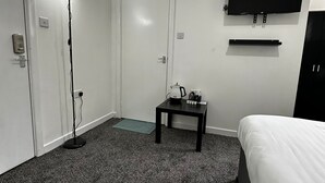 A hotel room with a bed, a desk with a kettle, a floor lamp, a TV mounted on the wall, and a door. - Blackwood Residence (Accrington)