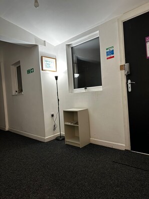A hallway with a black door, a window, a fire exit sign, and a framed picture on the wall. - Blackwood Residence (Accrington)