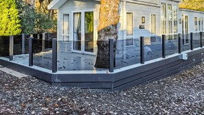 Une petite cabane à un seul étage, dotée d’un porche, entourée d’une clôture noire et d’arbres.