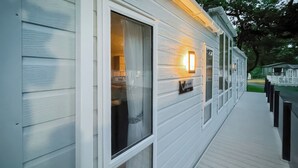 Une maison mobile blanche, dotée d’une terrasse en bois et d’un éclairage extérieur.