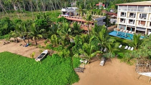 Un resort con varias construcciones, una piscina y una zona de playa con palmeras y sillas de descanso.