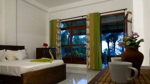Habitación de hotel con una cama, una ventana con cortinas, un florero con flores y una mesa con una taza.