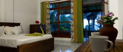 A hotel room with a bed, a window with curtains, a vase with flowers, and a table with a cup.