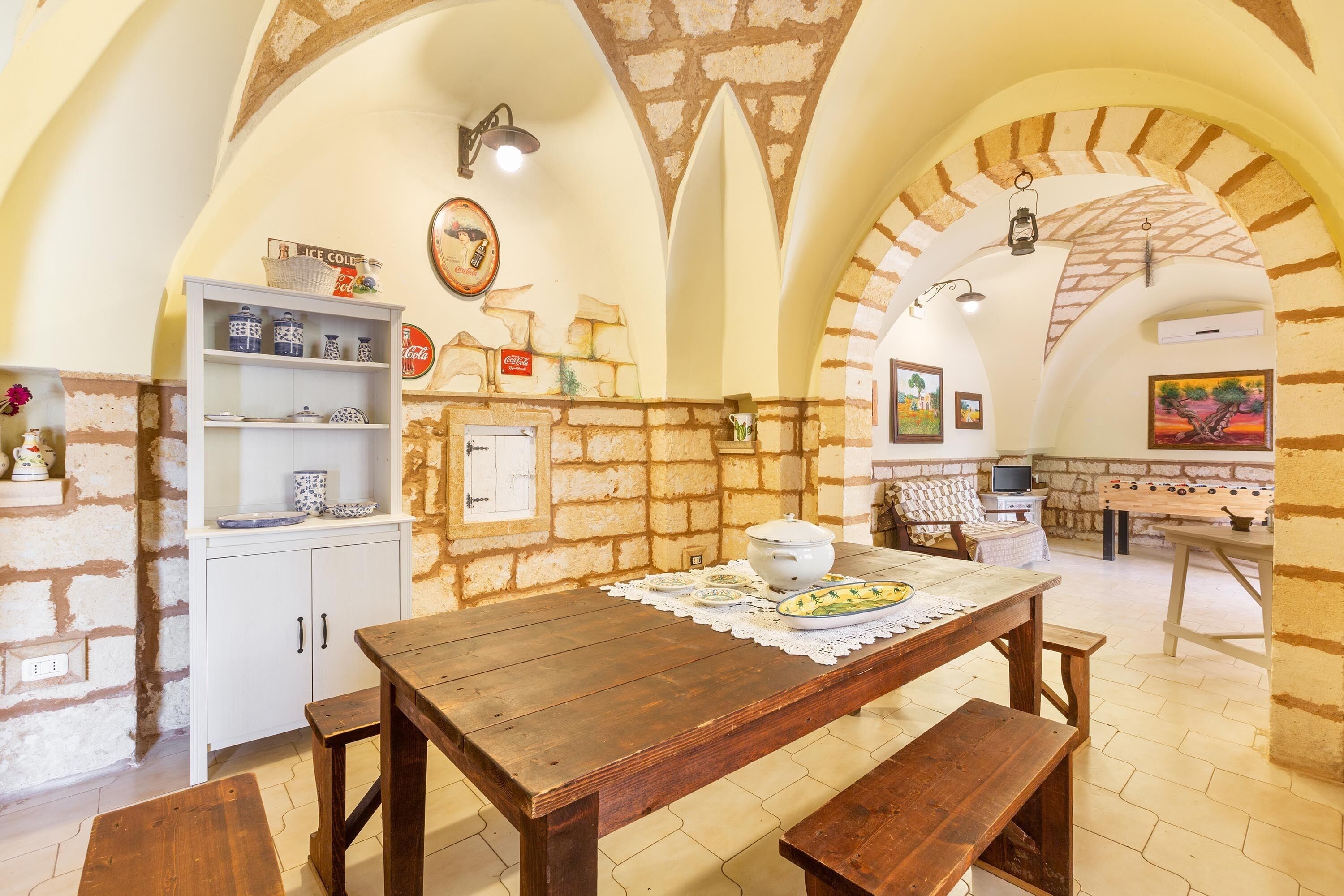 Uma cozinha rústica com mesa de madeira, armários brancos e parede de tijolos.