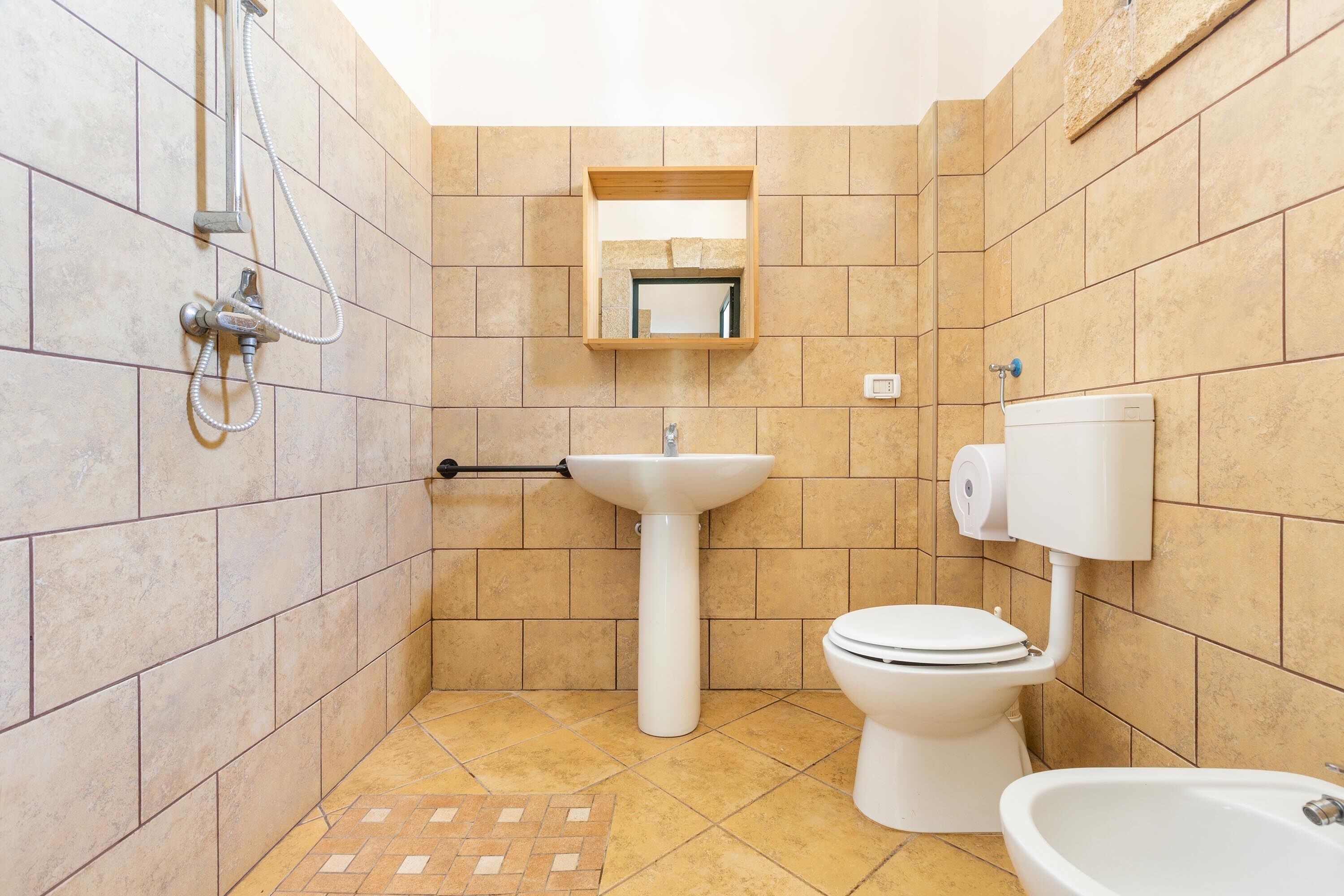 A bathroom with a shower, sink, toilet, and a small mirror.