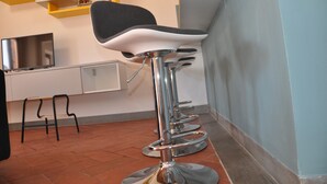 A row of bar stools with a black seat and chrome base, a white cabinet with a television, and a clock on the wall. - Vittoria apartment, 52 sqm, historic center of Florence   (Firenze)