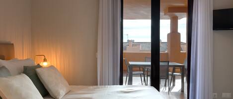A hotel room with a bed, a lamp, a TV, and a balcony with a table and chairs.