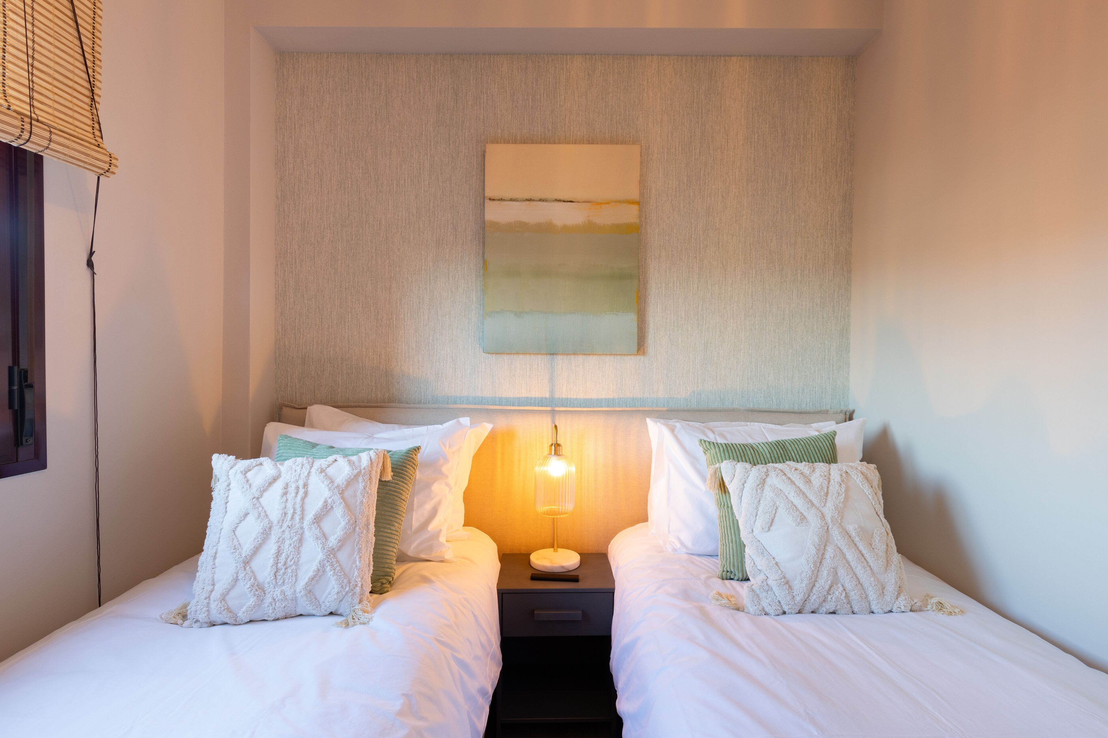 Una cama doble con ropa de cama blanca y dos almohadas, una mesita de noche con una lámpara y un cuadro en la pared.
