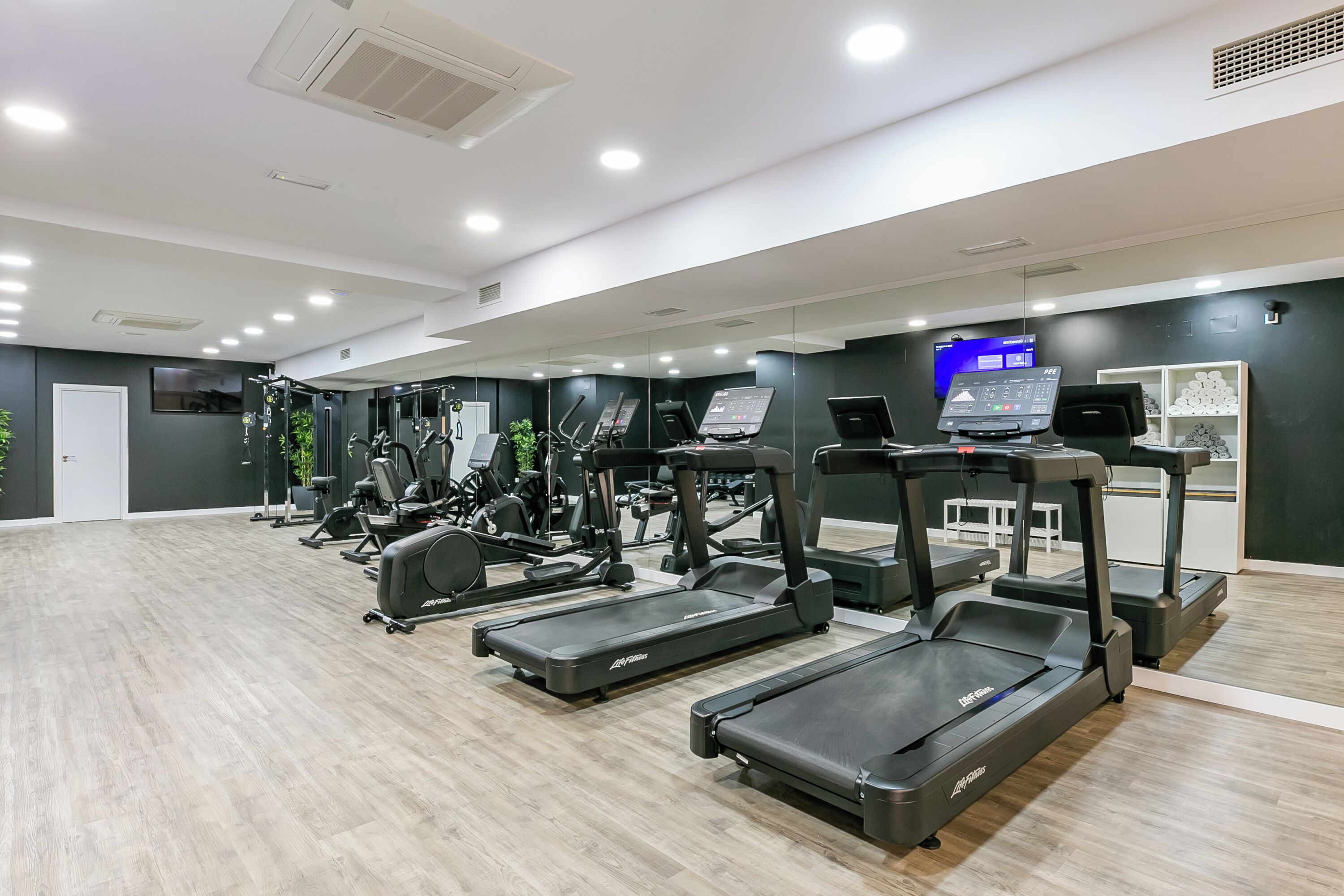 A modern gym with multiple treadmills, weight machines, and a digital display.