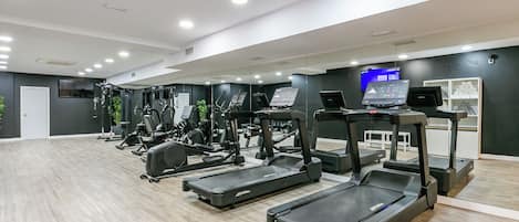 A modern gym with multiple treadmills, weight machines, and a digital display.