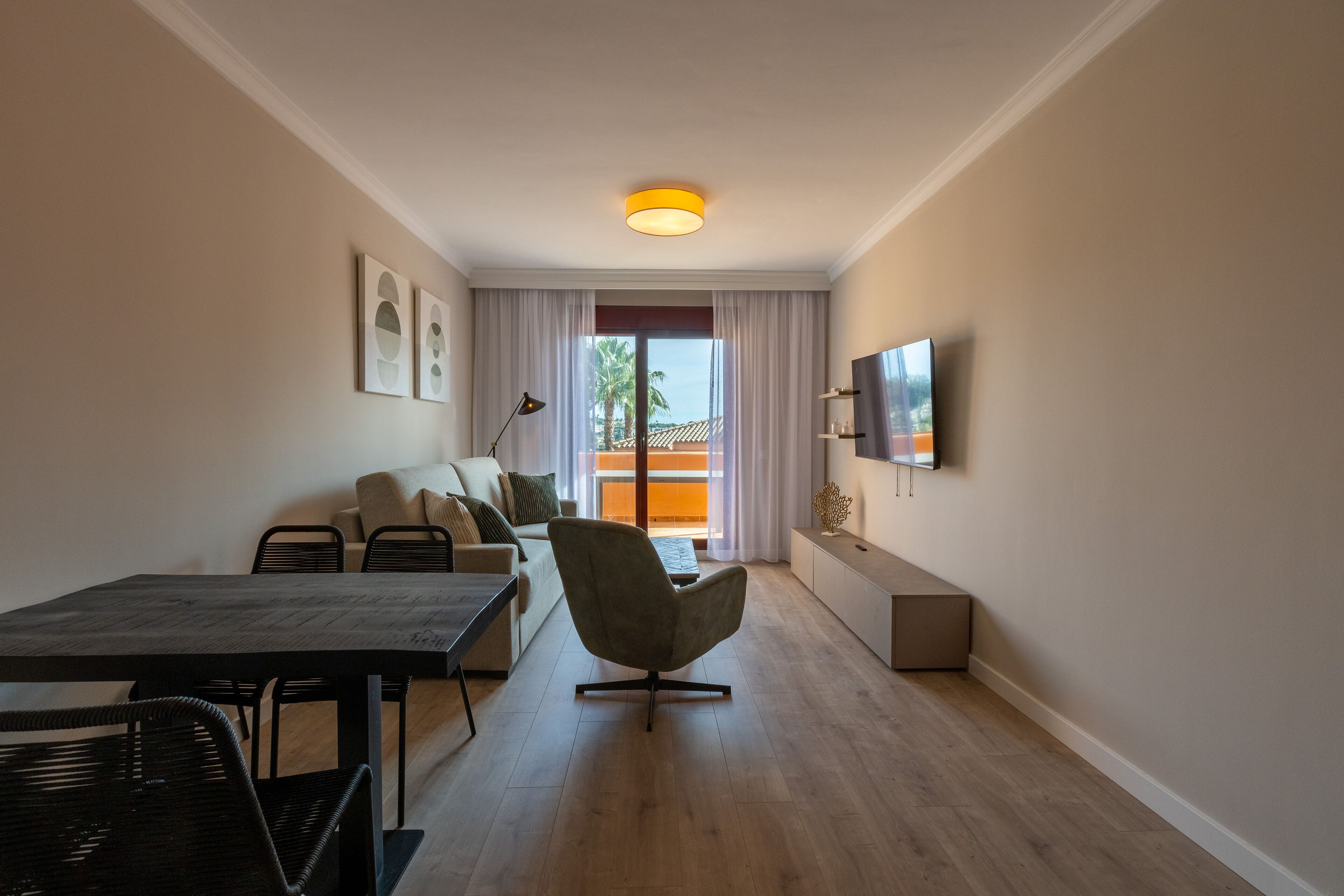Uma sala de estar moderna com uma mesa de jantar, um sofá, uma poltrona e uma TV fixada na parede.