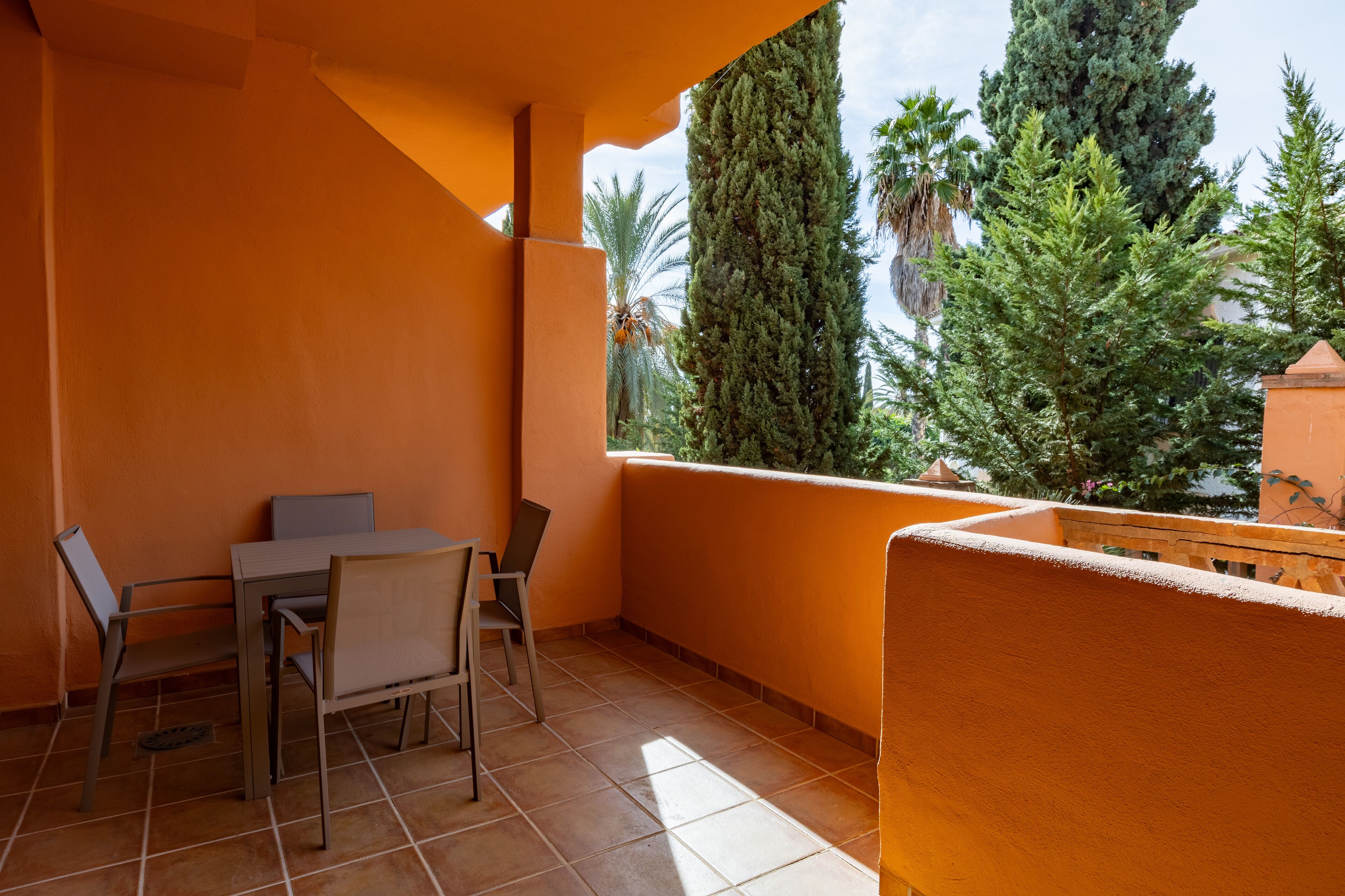 Ein Balkon mit Tisch und Stühlen, ein Fliesenboden und Blick auf Bäume sowie ein Gebäude.