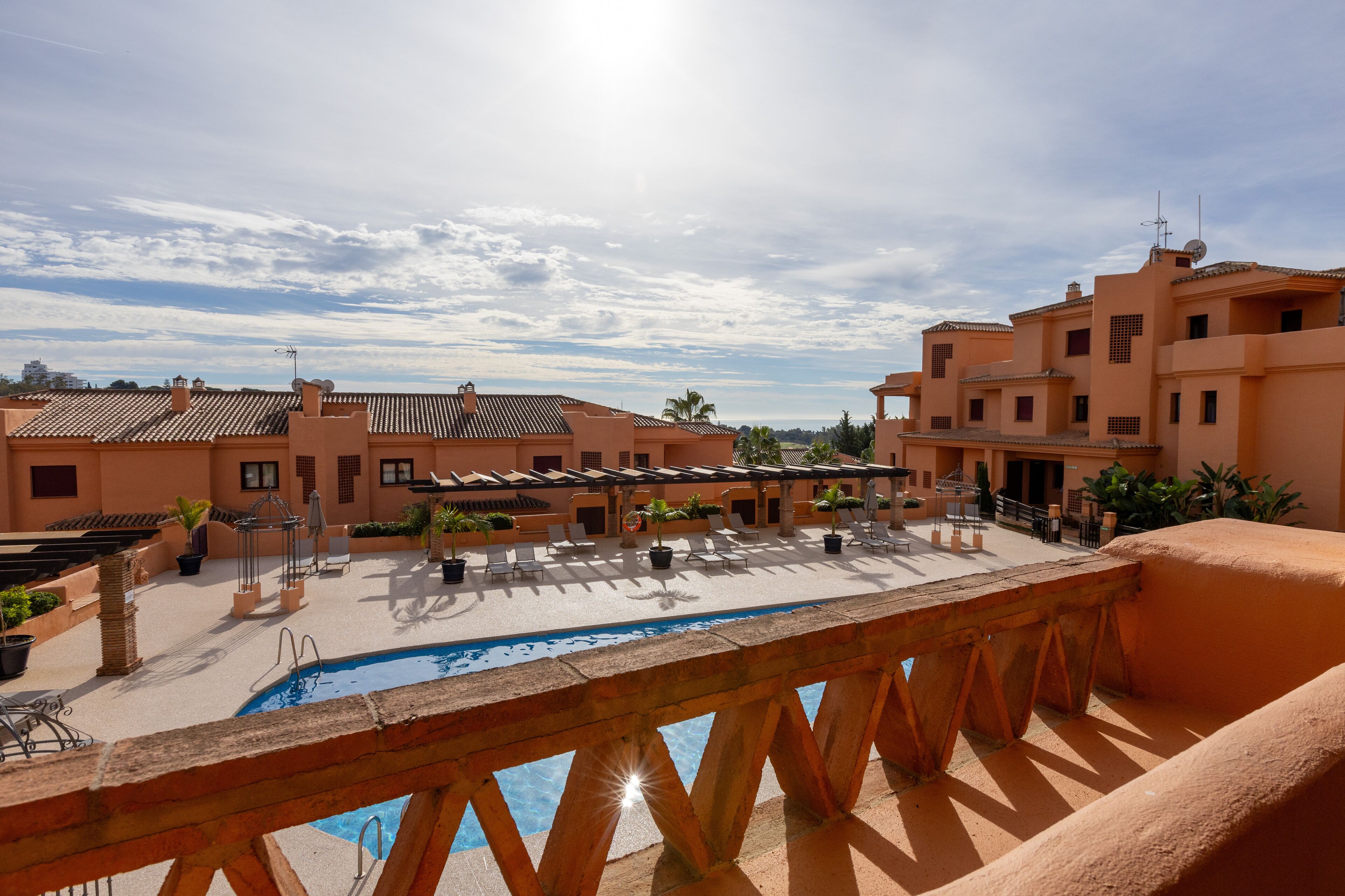 A rooftop pool area with lounge chairs and umbrellas, surrounded by buildings with terracotta roofs and balconies.