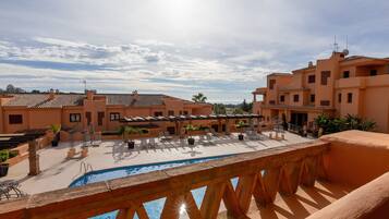 A rooftop pool area with lounge chairs and umbrellas, surrounded by buildings with terracotta roofs and balconies.