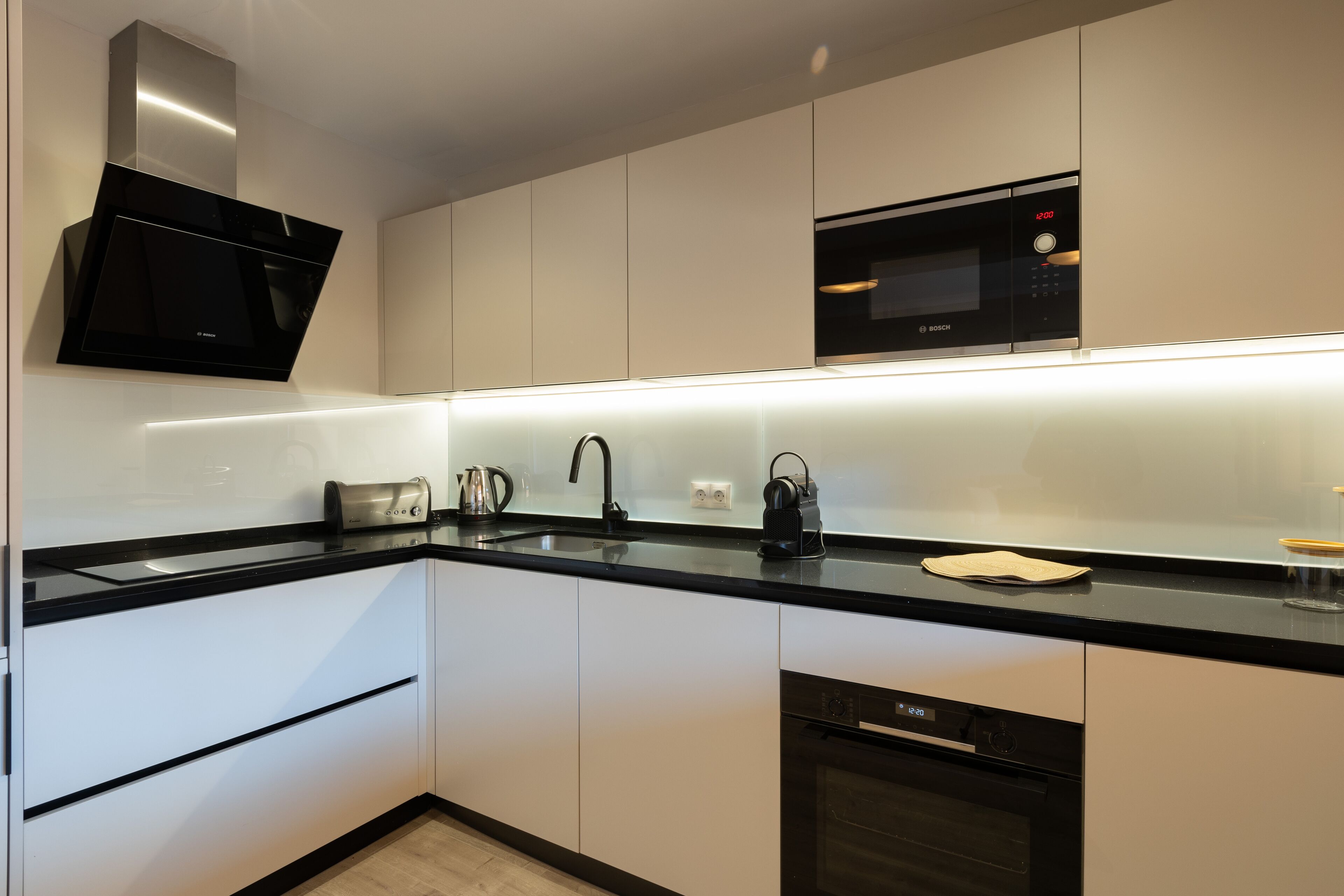 A modern kitchen with white cabinets, black countertops, a Bosch dishwasher, a microwave, and a stainless steel range hood.