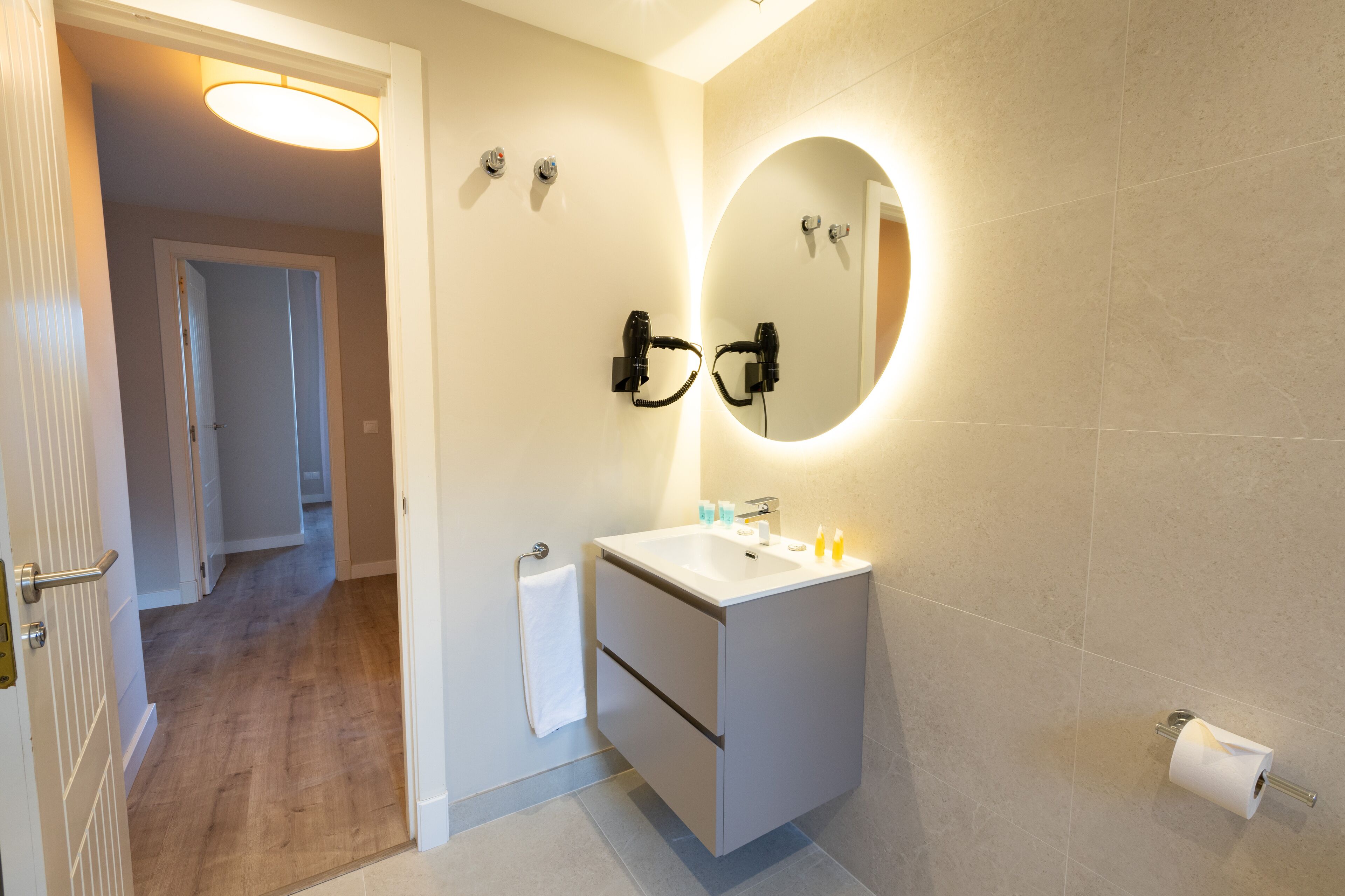 A modern bathroom with a white sink, a mirror, and a toilet paper holder.