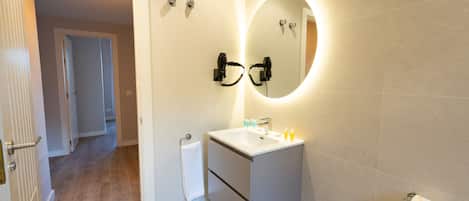 A modern bathroom with a white sink, a mirror, and a toilet paper holder.