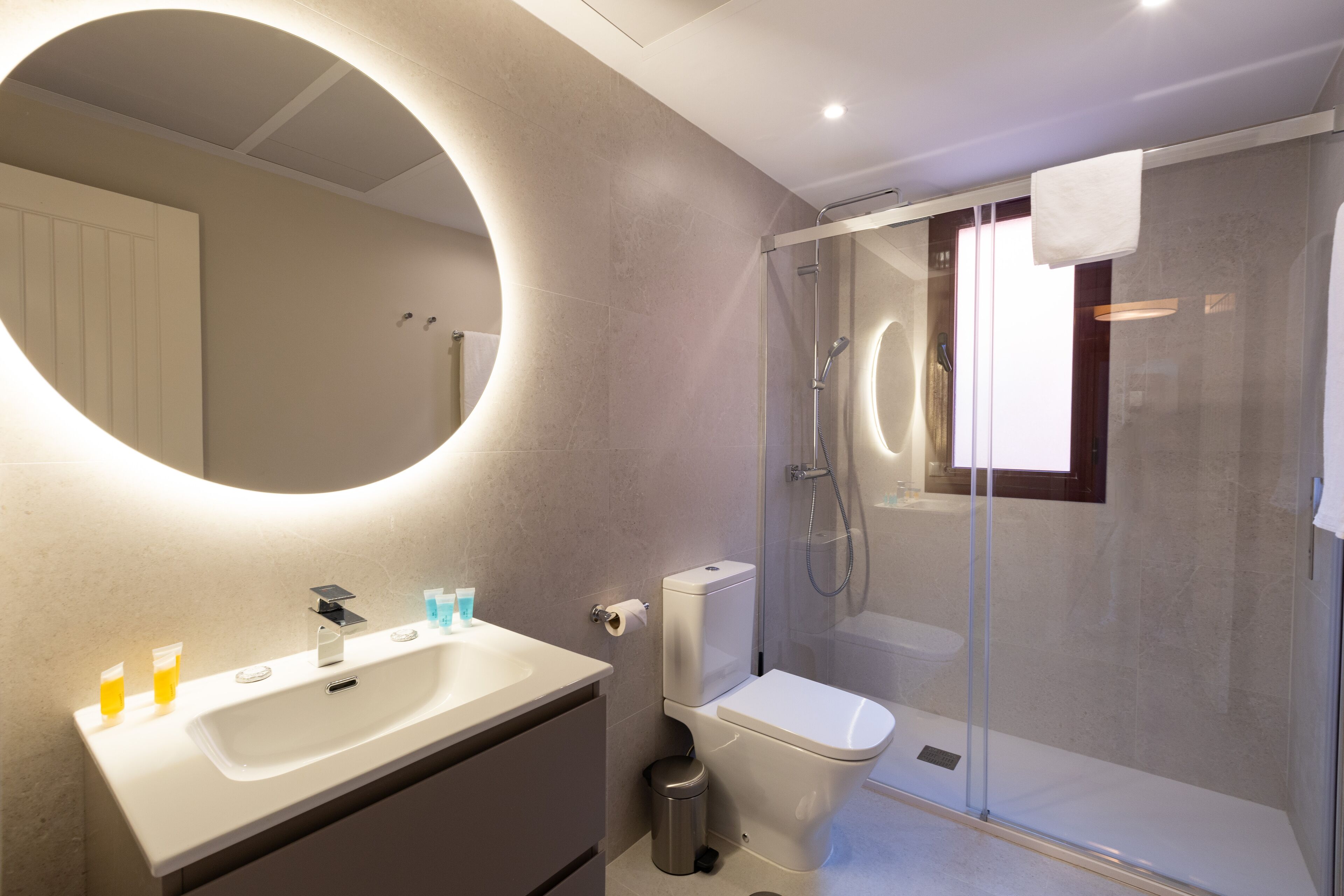 Un baño moderno con un espejo grande, un lavamanos, un inodoro y una ducha con mampara de vidrio.