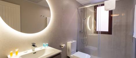 Un baño moderno con un espejo grande, un lavamanos, un inodoro y una ducha con mampara de vidrio.