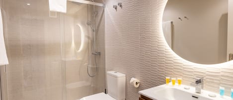 Une salle de bain moderne avec une douche à parois de verre, des toilettes, un lavabo avec des articles de toilette et un miroir.