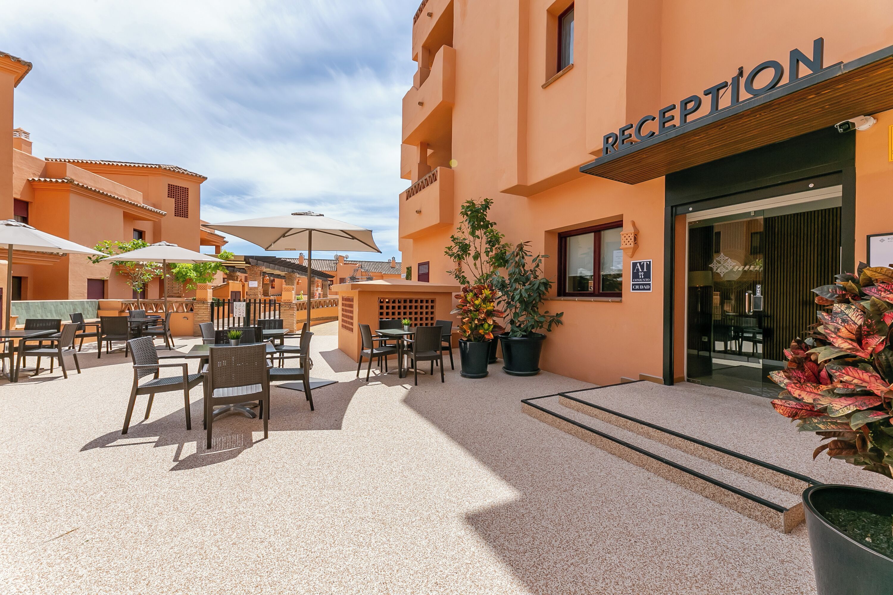 A hotel reception area with outdoor seating, potted plants, and a clear sky.