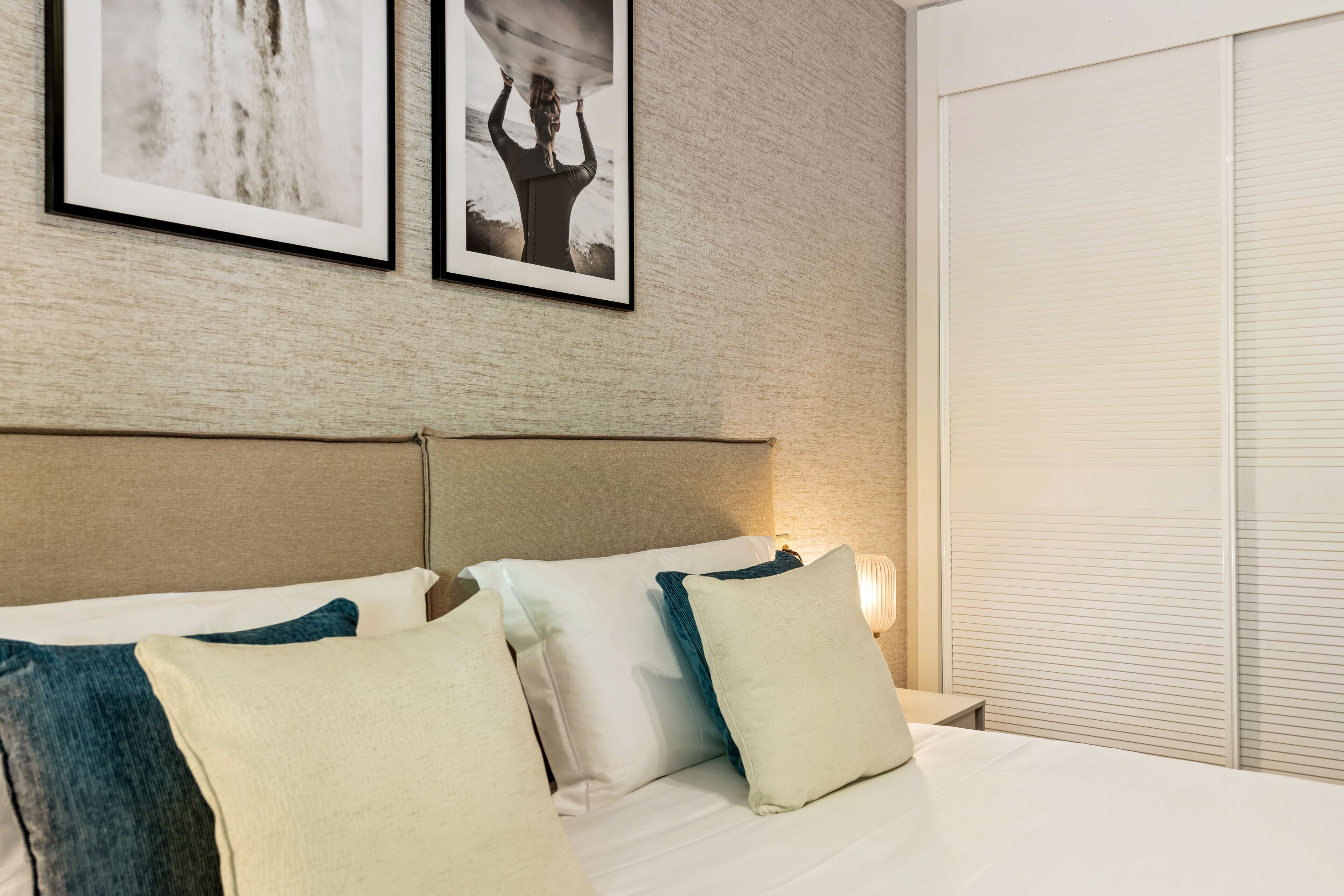 A neatly made bed with white and teal pillows, a headboard, and two framed pictures on the wall.