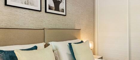 A neatly made bed with white and teal pillows, a headboard, and two framed pictures on the wall.