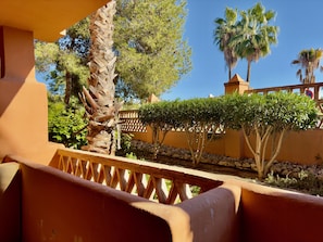 Una terraza con baranda de madera, palmeras y vista a un edificio de fachada amarilla.