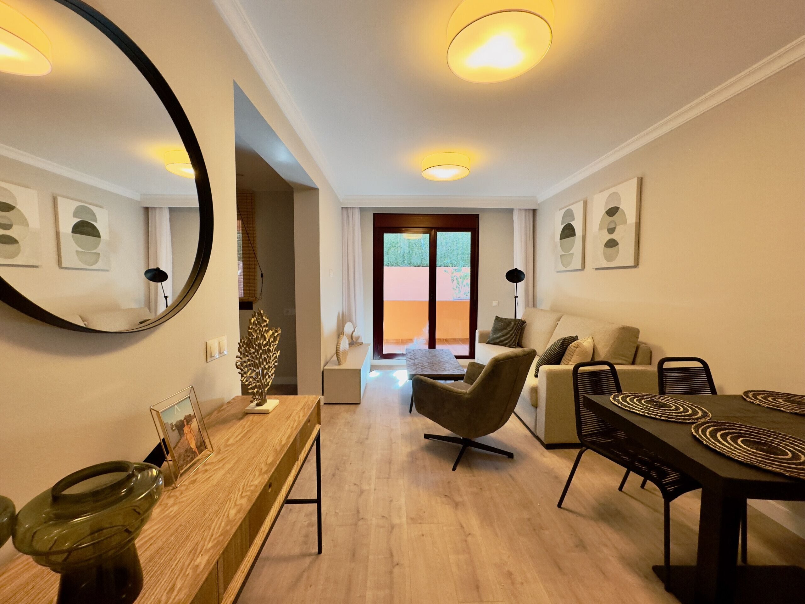 Un salon moderne avec un canapé, une table à manger et des chaises. Un grand miroir orne le mur, et une table basse en bois se trouve au centre de la pièce.