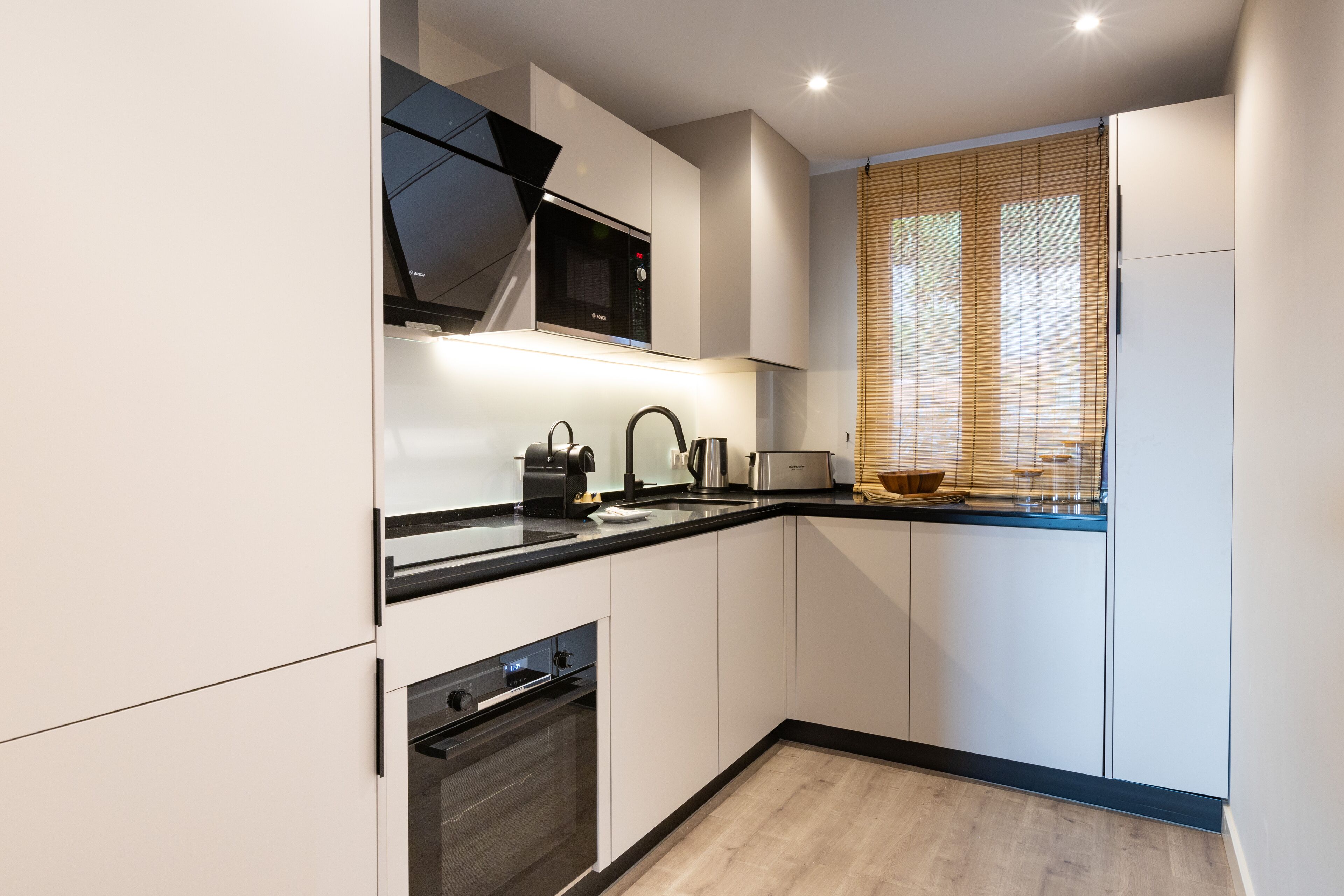 Una cocina moderna con armarios blancos, encimera negra, microondas, tostadora y ventana con persianas.