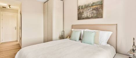 A bedroom with a large bed, a nightstand, a wardrobe, and a painting on the wall.