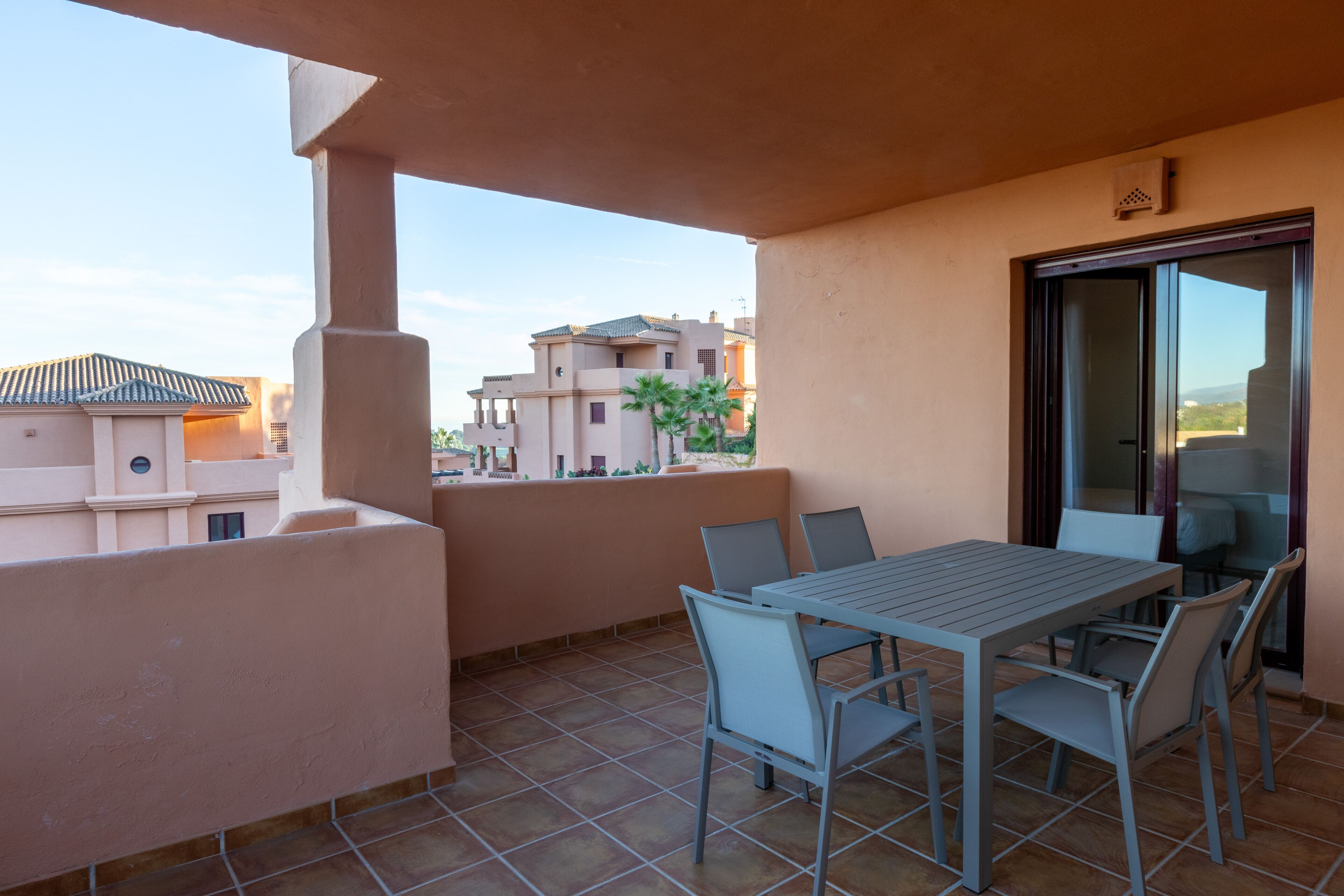 A balcony with a table and chairs, a sliding glass door, and a view of neighboring buildings.