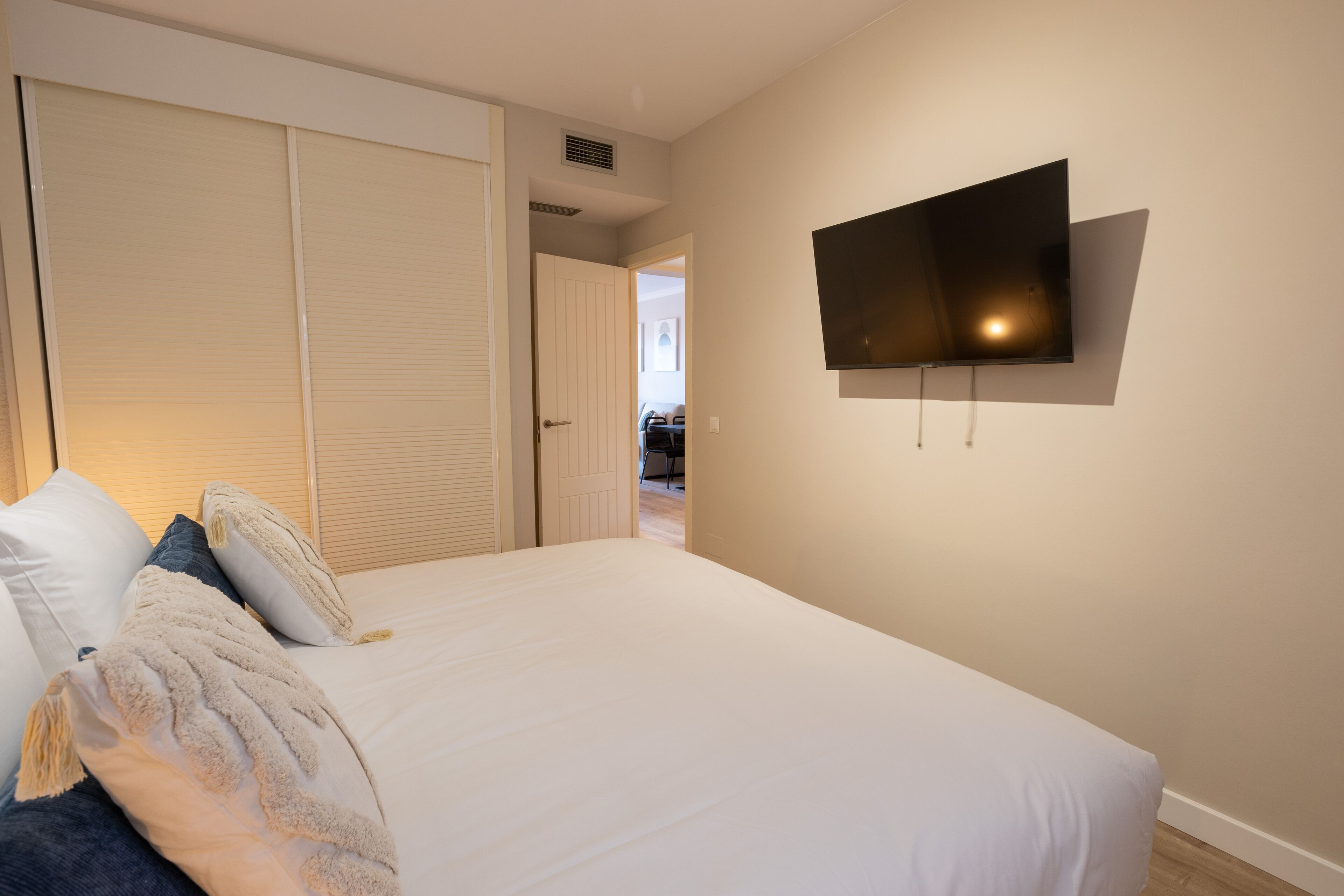 A bedroom with a bed, a TV mounted on the wall, and a closet with sliding doors.
