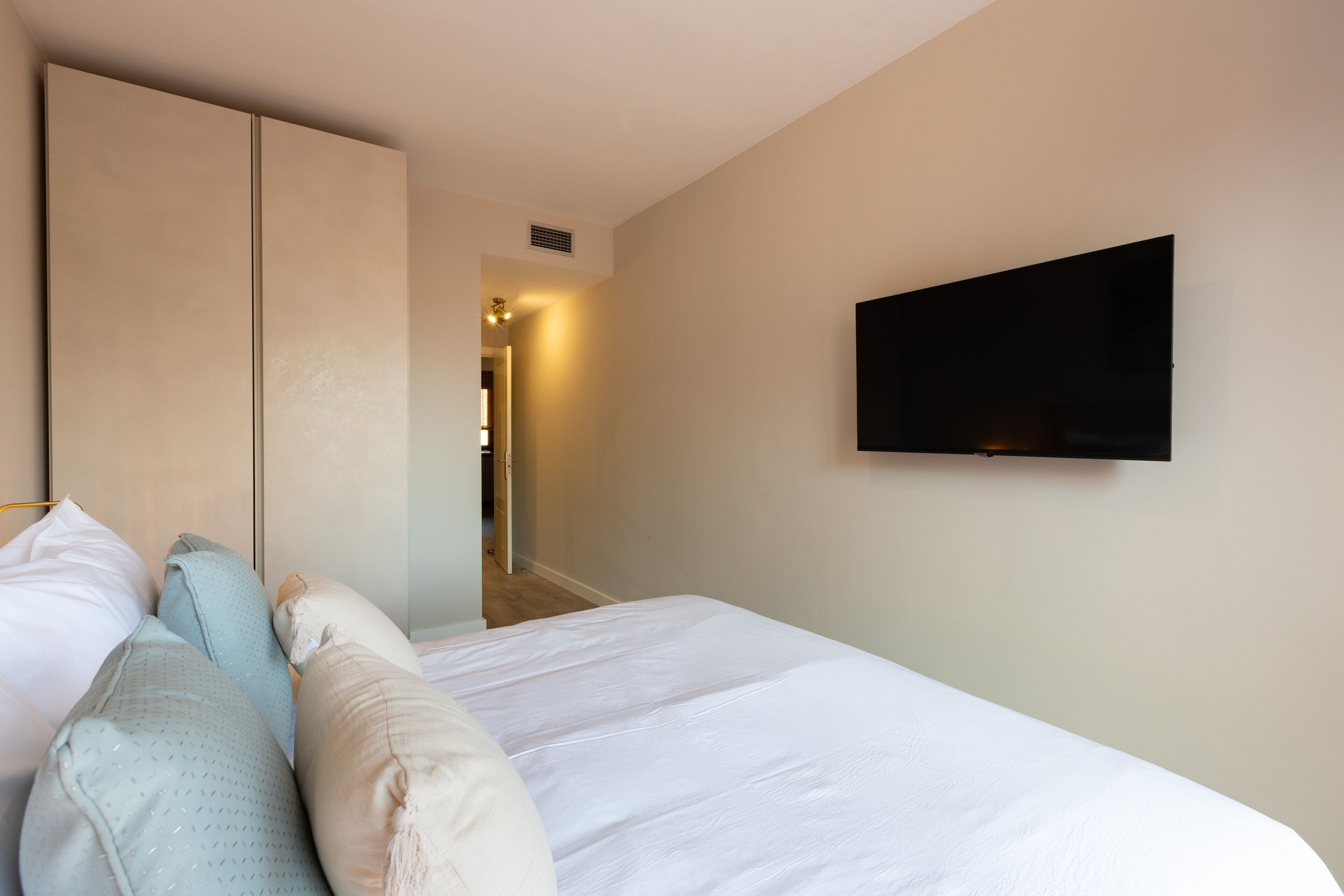 Une chambre d’hôtel avec un lit, des oreillers, une armoire et un téléviseur fixé au mur.