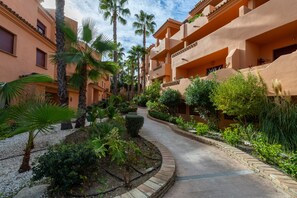 A courtyard with a curved pathway, palm trees, and a building with balconies. - Royal Marbella Golf Resort (Benahavis)